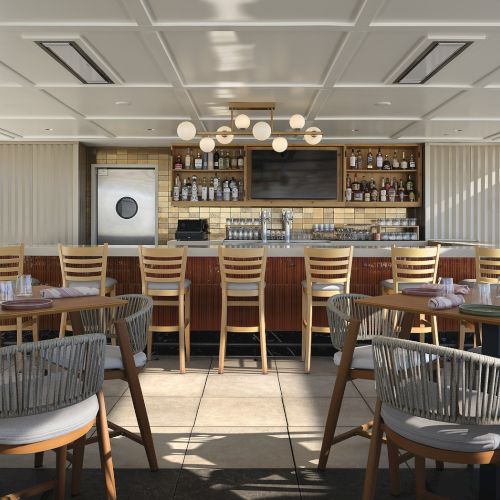 Outdoor bar with a wooden counter, globe lights, shelves of bottles, and neatly set tables and chairs.